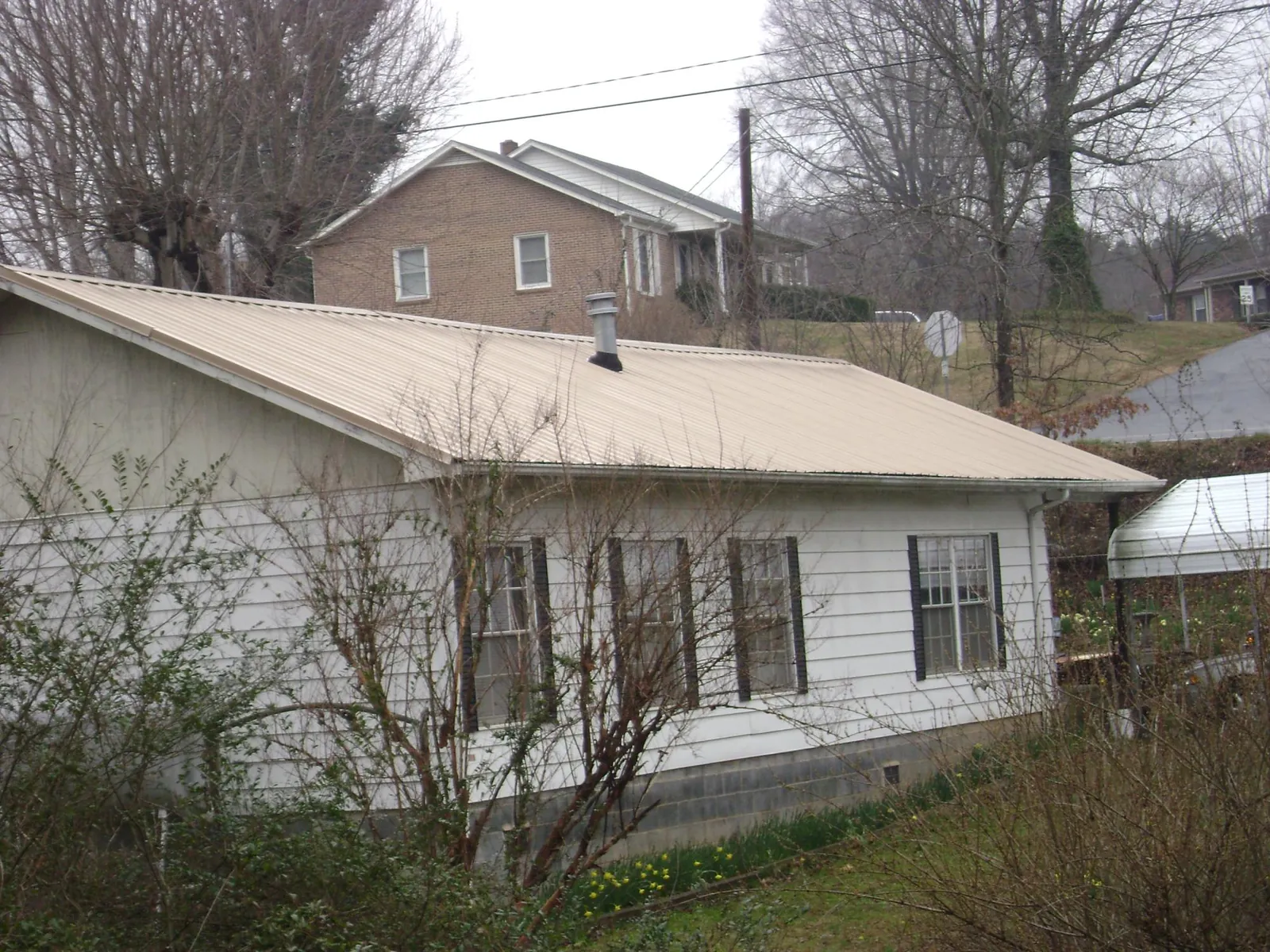 Tan metal roof on a white sided house set into a hillside — Commercial Roofing by Roofing Brothers in Seminole