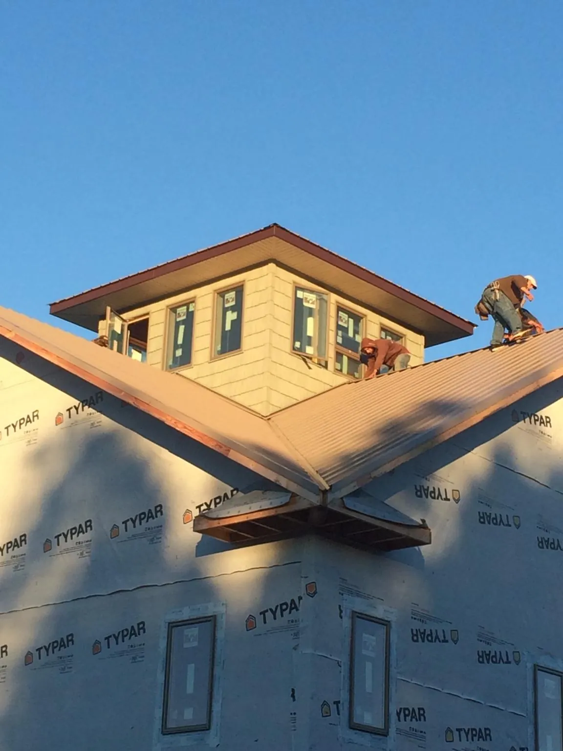 Roofers working around a rooftop cupola on a new metal roof at sunset in Seminole